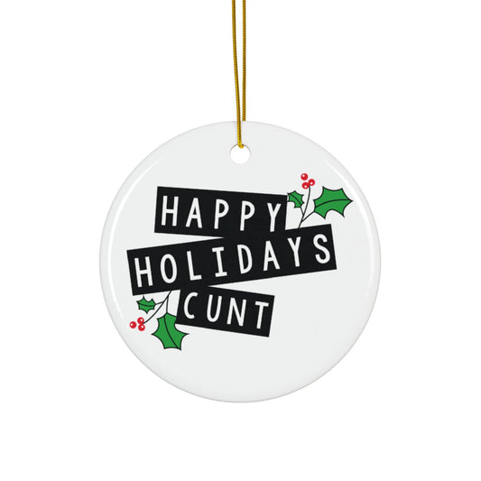 Round white ceramic ornament with 'Happy Holidays Cunt' text and holly design, hanging on a gold string.